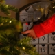 A child hand in a red sweater opens the advent calendar near Christmas tree .