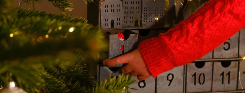 A child hand in a red sweater opens the advent calendar near Christmas tree .